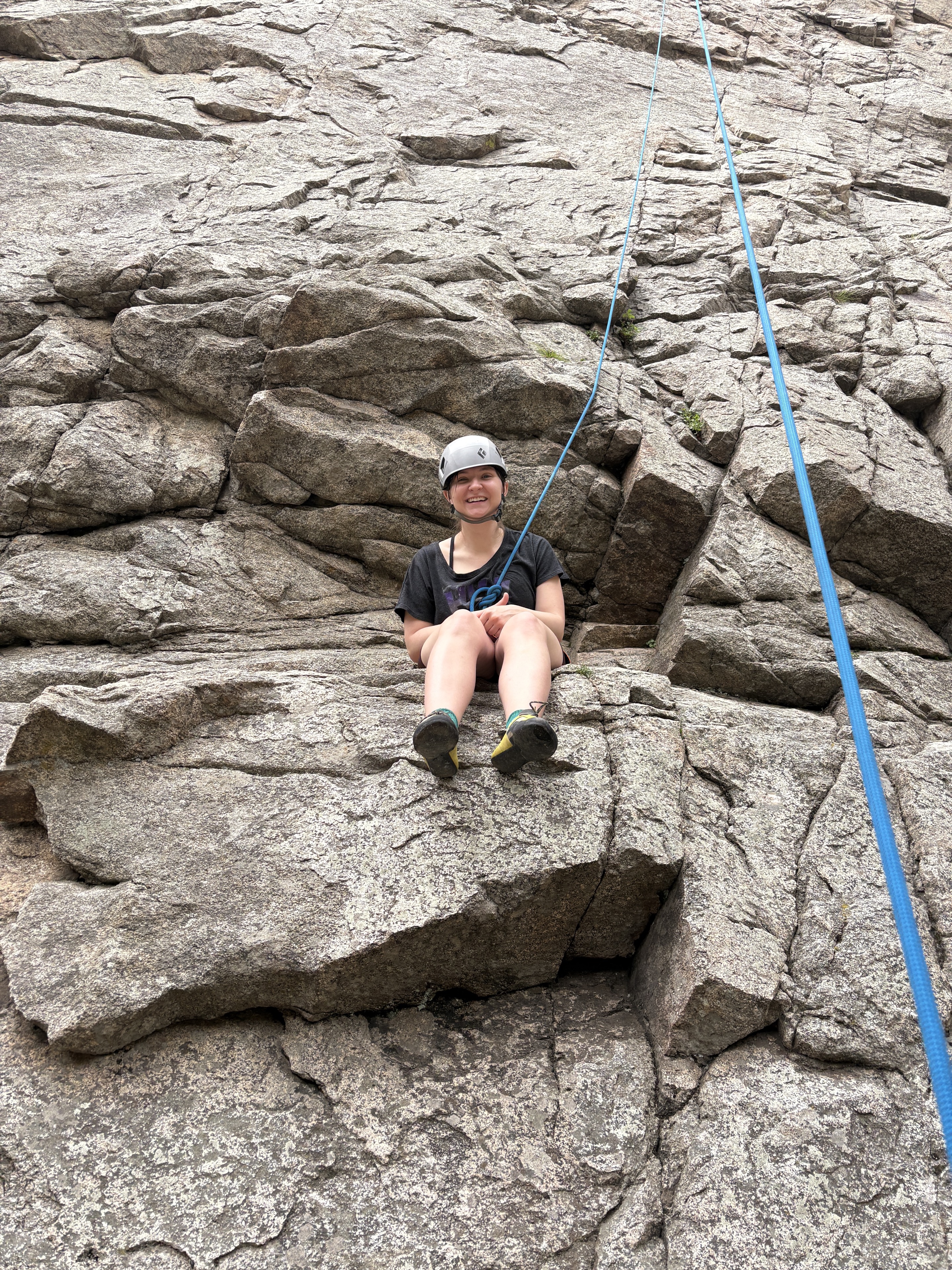 Smiling helmeted climber on a rock ledge with a climbing rope