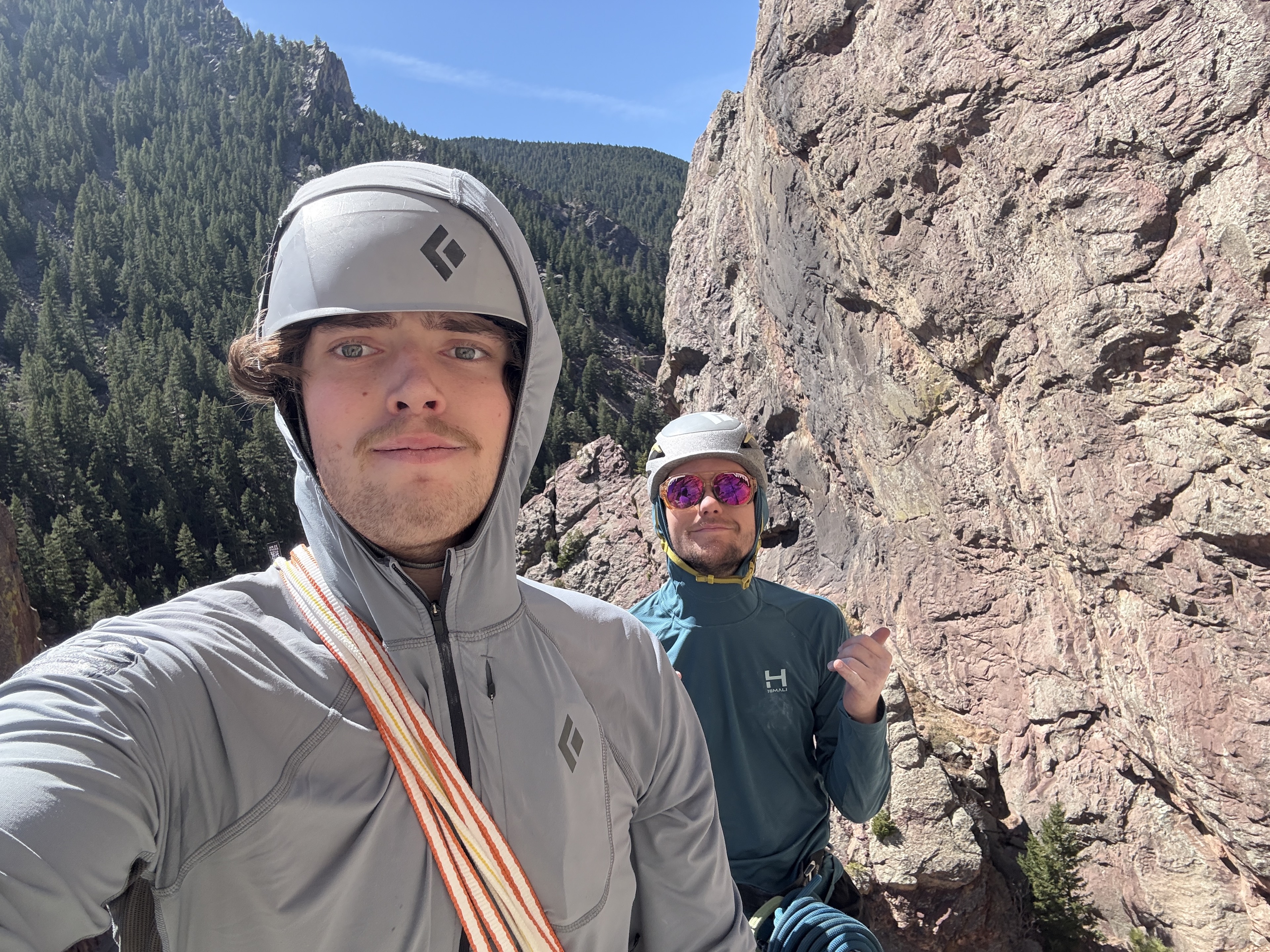 Two helmeted climbers beside a rock wall in a wooded canyon